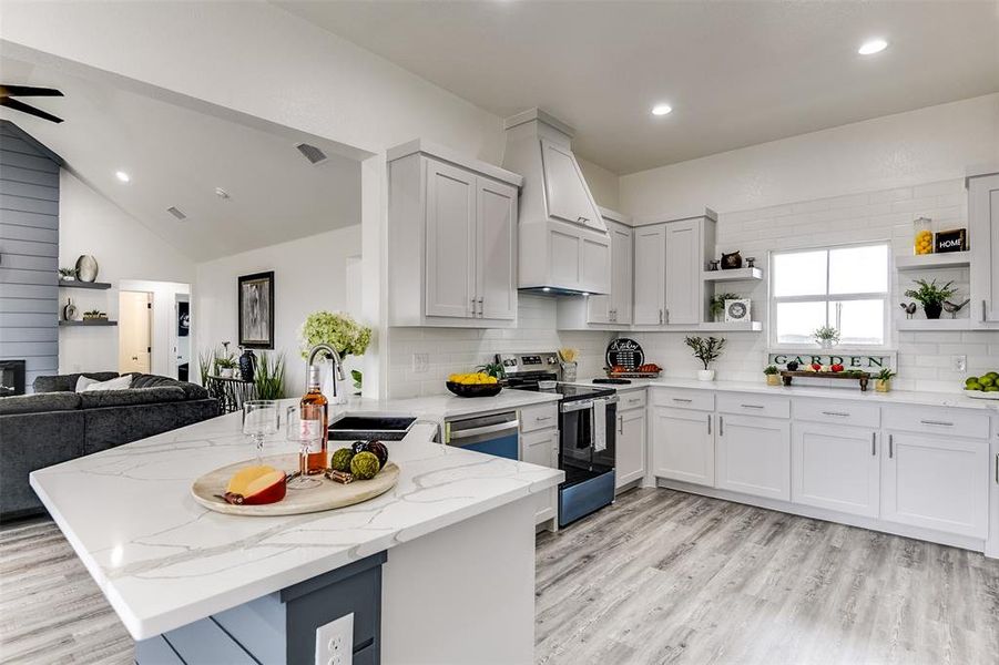 Kitchen with stainless steel appliances, open floor plan, a sink, light stone countertops, and a peninsula