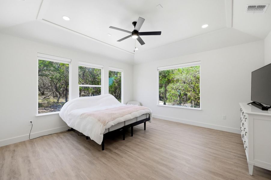 Generous windows frame peaceful wooded views from this spacious bedroom with tray ceilings.
