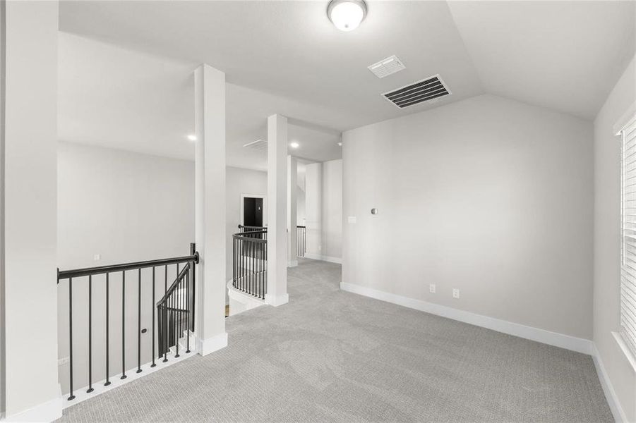 Spacious open loft area with vaulted ceilings, light gray carpeting, and white baseboards Spacious open loft area with vaulted ceilings, light gray carpeting, and white baseboards