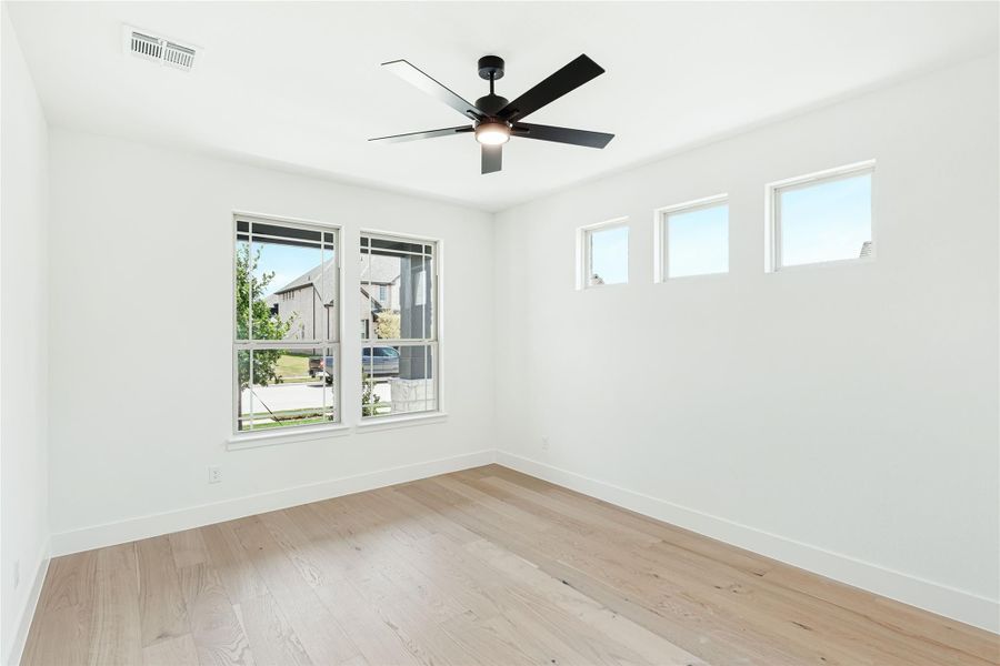 Empty room with light hardwood floors, white walls, black ceiling fan, and multiple windows Empty room with light hardwood floors, white walls, black ceiling fan, and multiple windows