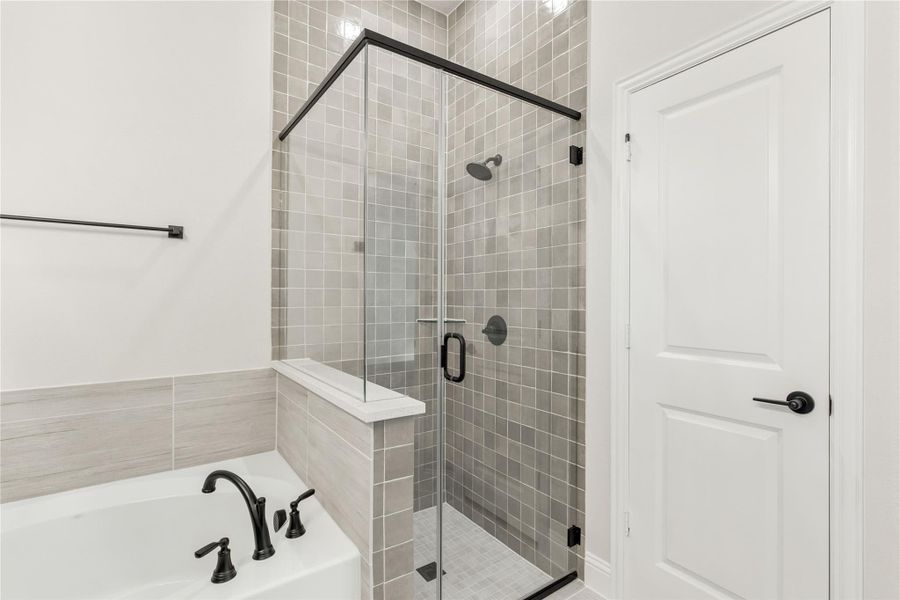 Bathroom with glass-enclosed walk-in shower, gray tile walls, and soaking tub with black fixtures Bathroom with glass-enclosed walk-in shower, gray tile walls, and soaking tub with black fixtures