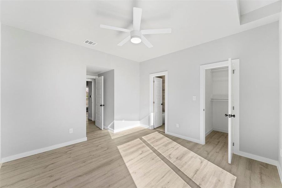 Unfurnished bedroom with a walk in closet, light wood-style flooring, and ceiling fan