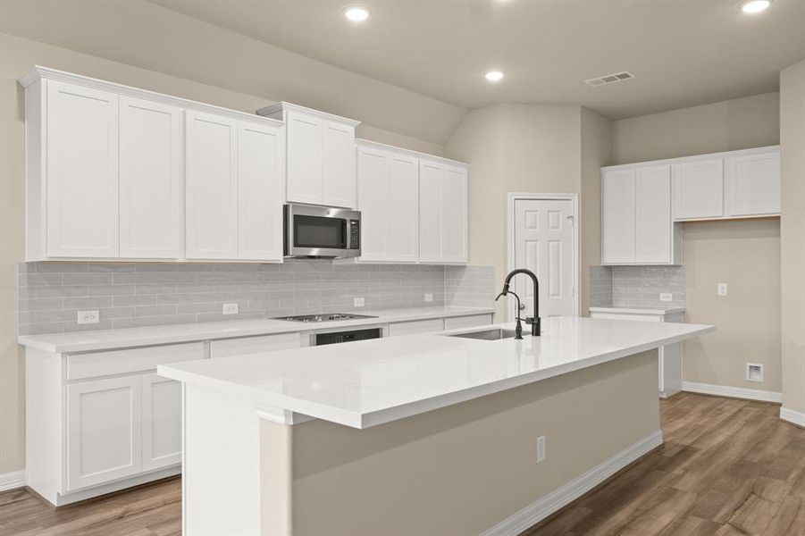 This light and bright kitchen features a large quartz island, white cabinets, a large sink overlooking your family room, recessed lighting, and beautiful backsplash.