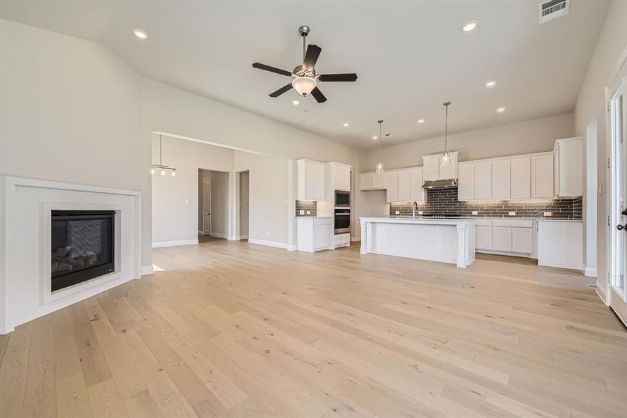 Kitchen featuring light wood-type flooring, a kitchen island with sink, pendant lighting, white cabinetry, and appliances with stainless steel finishes