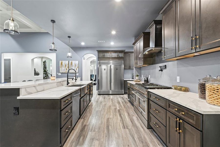 Kitchen with hanging light fixtures, high end appliances, light stone countertops, wall chimney exhaust hood, and recessed lighting