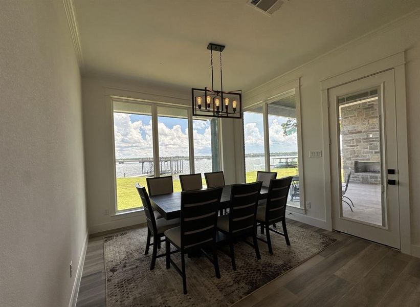 Dining space featuring dark wood finished floors, a chandelier, a water view, healthy amount of natural light, and crown molding Dining space featuring dark wood finished floors, a chandelier, a water view, healthy amount of natural light, and crown molding