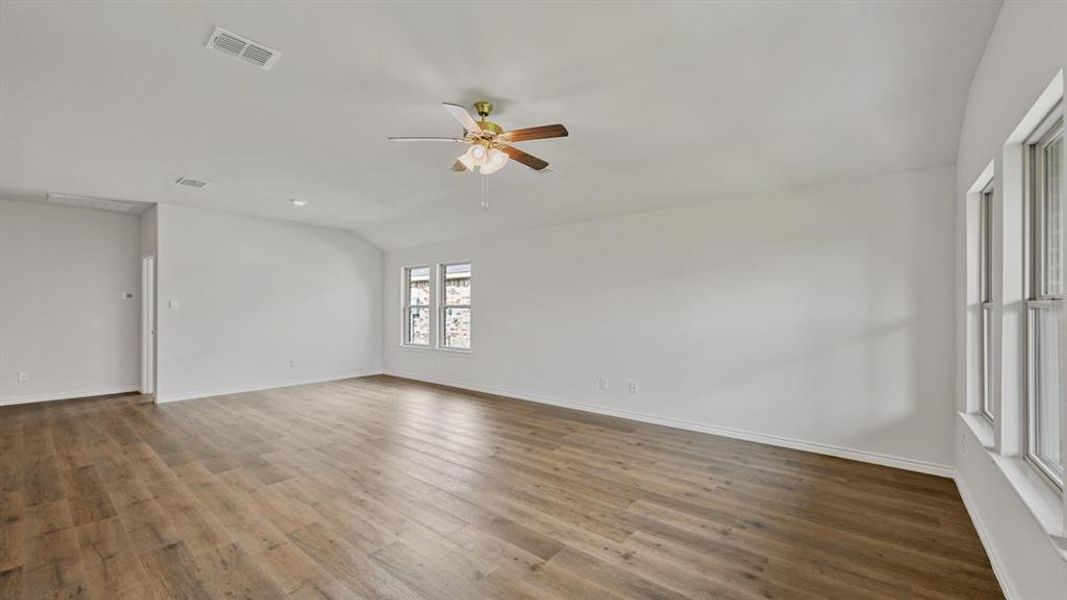 Spacious interior room featuring wood-finish flooring, white walls, and a ceiling fan with integrated lighting Spacious interior room featuring wood-finish flooring, white walls, and a ceiling fan with integrated lighting