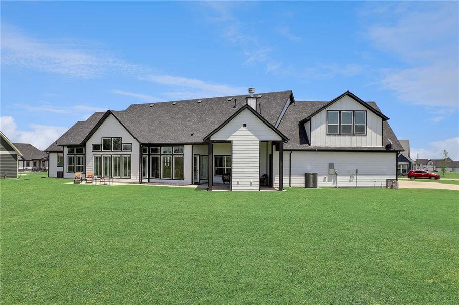 Rear view of house featuring board and batten siding, a lawn, a patio, and roof with shingles Rear view of house featuring board and batten siding, a lawn, a patio, and roof with shingles