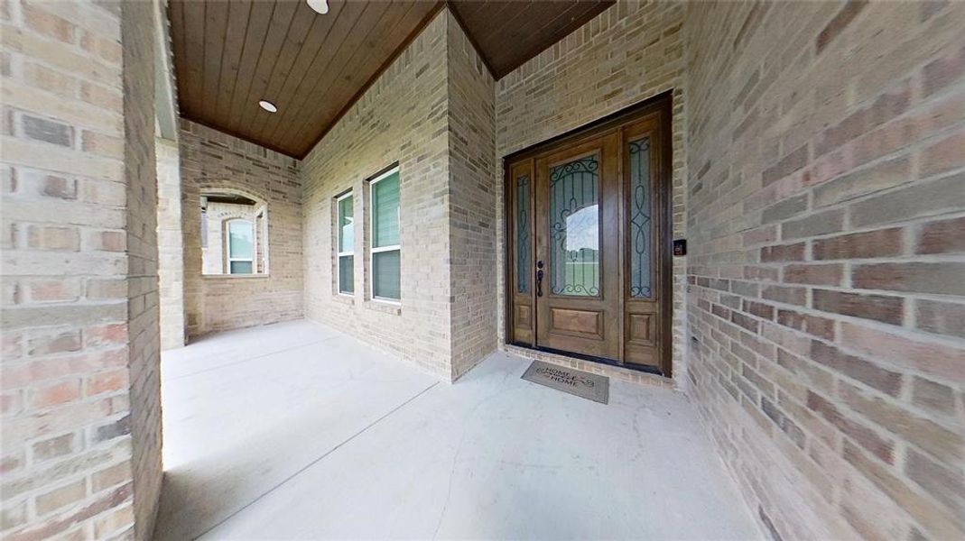 Covered entryway featuring a wood-finish door with decorative glass inserts, brick exterior, and a wood-paneled ceiling Covered entryway featuring a wood-finish door with decorative glass inserts, brick exterior, and a wood-paneled ceiling