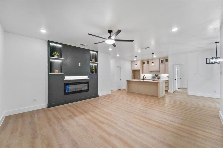 Spacious interior featuring wood-finish flooring, a contemporary fireplace with integrated shelving, recessed lighting, and a modern ceiling fan Spacious interior featuring wood-finish flooring, a contemporary fireplace with integrated shelving, recessed lighting, and a modern ceiling fan