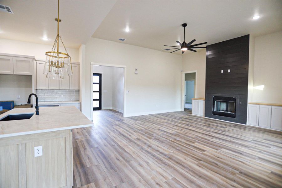 Kitchen featuring light wood-style floors, tasteful backsplash, open floor plan, a center island with sink, and a fireplace