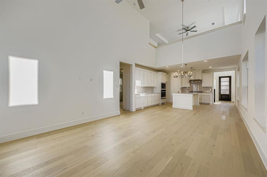 Unfurnished living room featuring light wood-style flooring, a chandelier, a ceiling fan, and a towering ceiling
