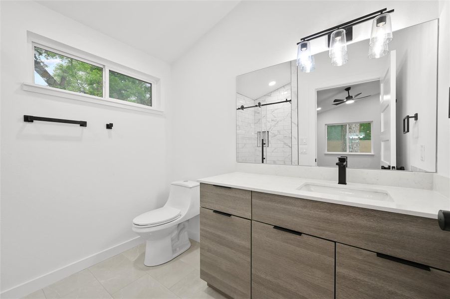 Bathroom with vaulted ceiling, a stall shower, toilet, vanity, and ceiling fan