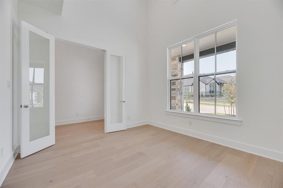 Empty room featuring healthy amount of natural light, light wood-type flooring, french doors, and a towering ceiling