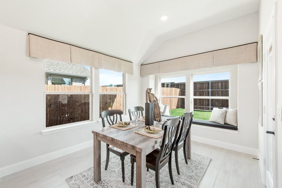 Bright dining area with wood table, black chairs, window seat, and large windows overlooking backyard fence Bright dining area with wood table, black chairs, window seat, and large windows overlooking backyard fence