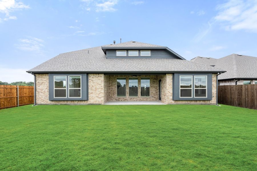 Rear view of single-story brick home with large windows, covered patio, and fenced backyard with green lawn