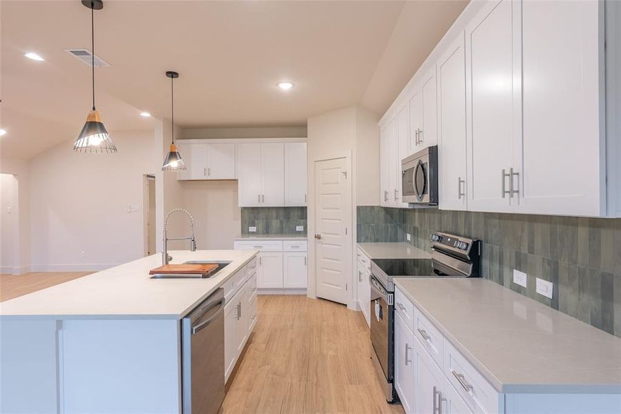 Kitchen featuring appliances with stainless steel finishes, light wood-type flooring, hanging light fixtures, tasteful backsplash, and recessed lighting