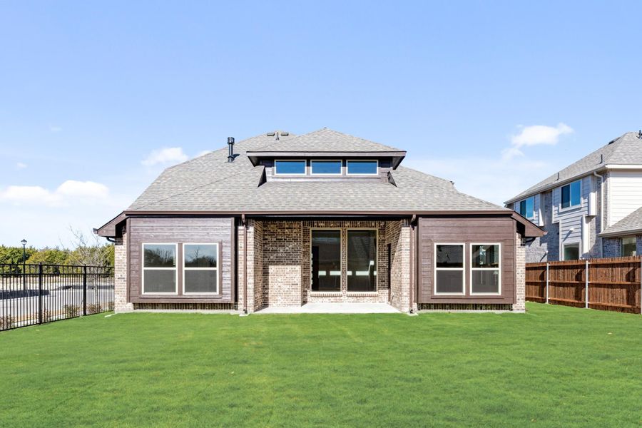 Rear exterior of single-story brick home with hip roof, large windows, patio, and fenced backyard with green lawn Rear exterior of single-story brick home with hip roof, large windows, patio, and fenced backyard with green lawn