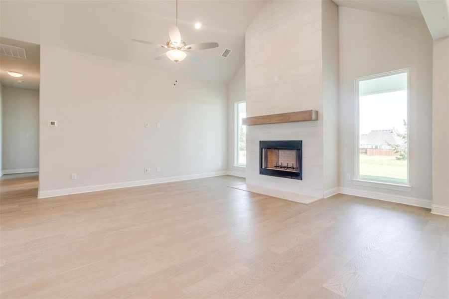 Unfurnished living room featuring a fireplace, ceiling fan, light hardwood / wood-style floors, and high vaulted ceiling