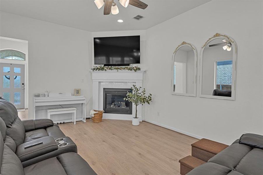 Living area featuring wood-finish flooring, a corner fireplace with a white mantel, and an arched entryway Living area featuring wood-finish flooring, a corner fireplace with a white mantel, and an arched entryway
