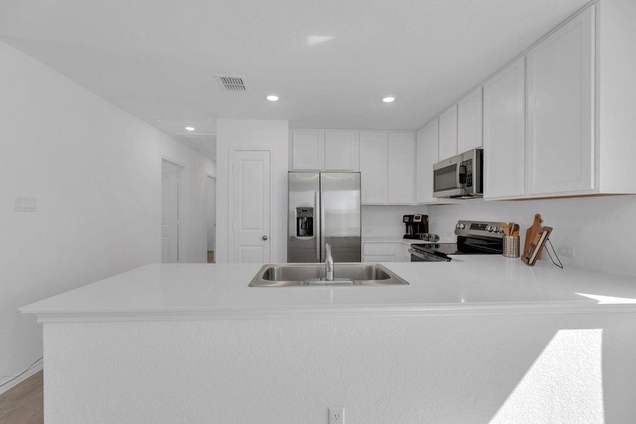 Open kitchen featuring a peninsula, stainless steel appliances, white cabinetry, and recessed lighting.
