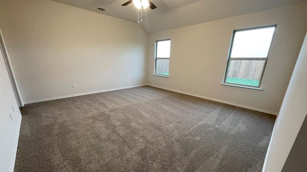 Spacious room featuring vaulted ceilings, a ceiling fan with integrated lighting, two windows, and light-toned carpet flooring