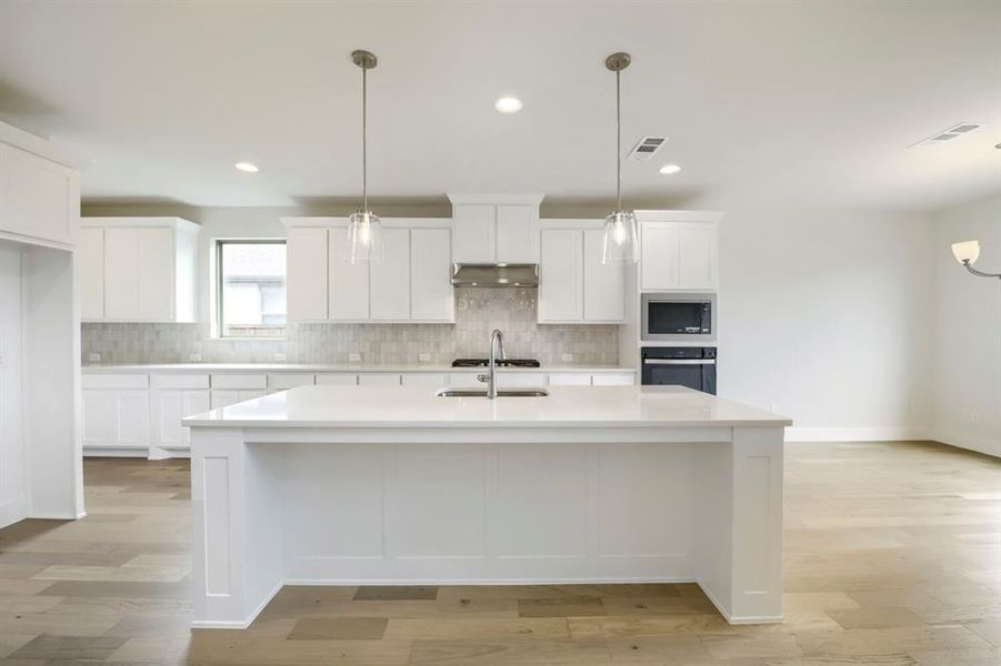Kitchen featuring a large island with sink, white shaker-style cabinetry, mosaic tile backsplash, and stainless steel appliances including a built-in microwave and oven Kitchen featuring a large island with sink, white shaker-style cabinetry, mosaic tile backsplash, and stainless steel appliances including a built-in microwave and oven