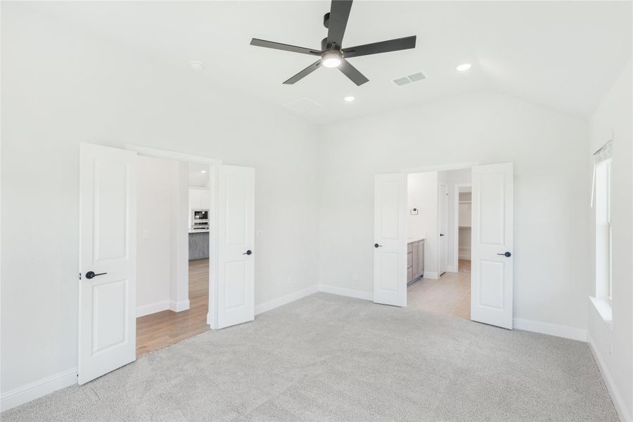 Empty bedroom with carpet, ceiling fan, and open doors leading to bathroom and walk-in closet