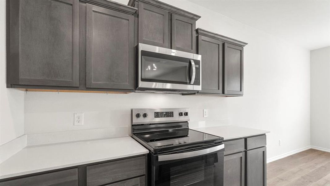 The kitchen features dark wood cabinetry, white countertops, and stainless steel appliances including a microwave and an electric range