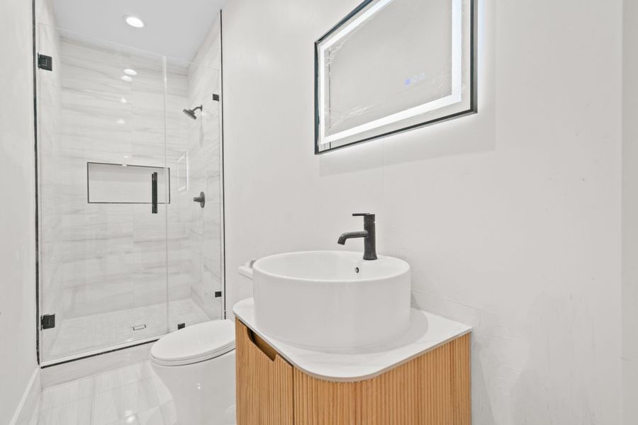 This luxurious bathroom showcases refined contemporary design and impeccable attention to detail. A striking vessel sink rests atop a custom fluted-wood vanity, complemented by elegant modern fixtures and a sleek quartz countertop . The expansive frameless glass- enclosed shower features designer telework, recessed niches and premium fixtures.