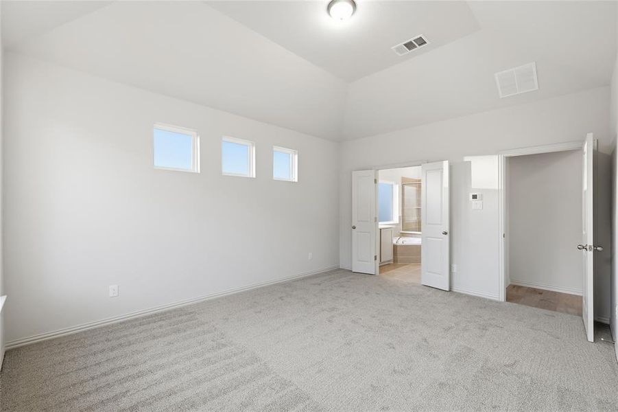 Unfurnished bedroom with connected bathroom, light carpet, and lofted ceiling