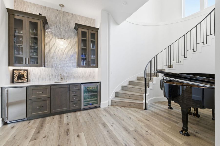 Indoor wet bar featuring glass fronted cabinets, stainless steel built in fridge, beverage cooler, and dark wood finish cabinetry