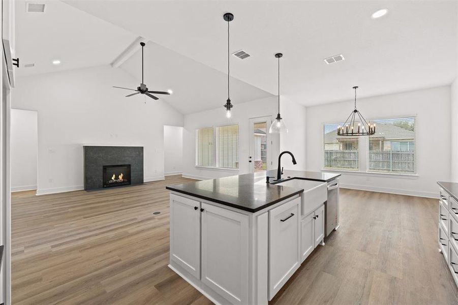 Kitchen with a high ceiling, white cabinets, a fireplace with flush hearth, light wood-style flooring, and a kitchen island with sink