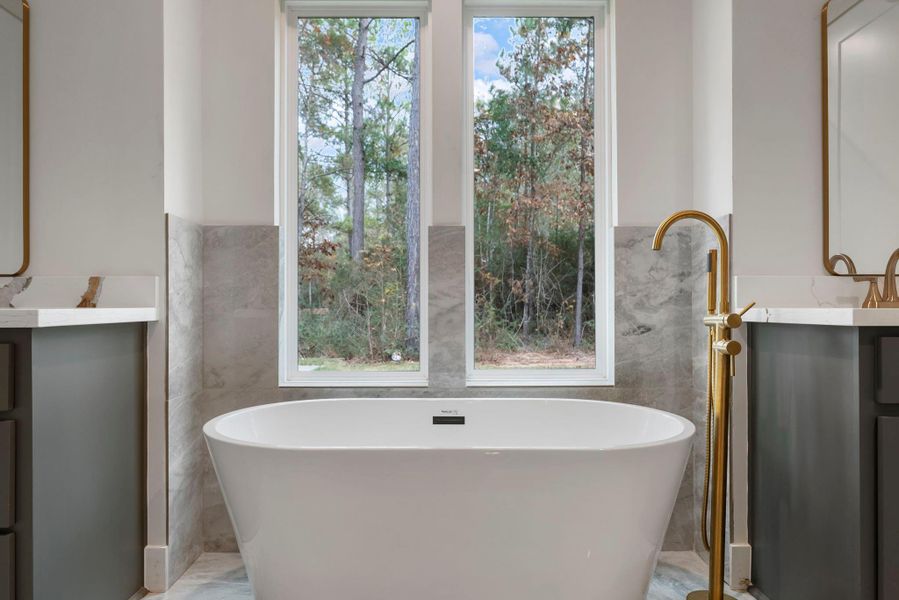 The modern freestanding tub with a sleek gold faucet with windows that  offer a view of the wooded outdoors, creating a serene atmosphere and privacy.