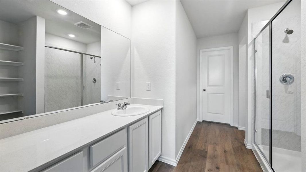 Bathroom featuring a single vanity with a white countertop, built-in shelving, a glass-enclosed shower, and wood-finish flooring