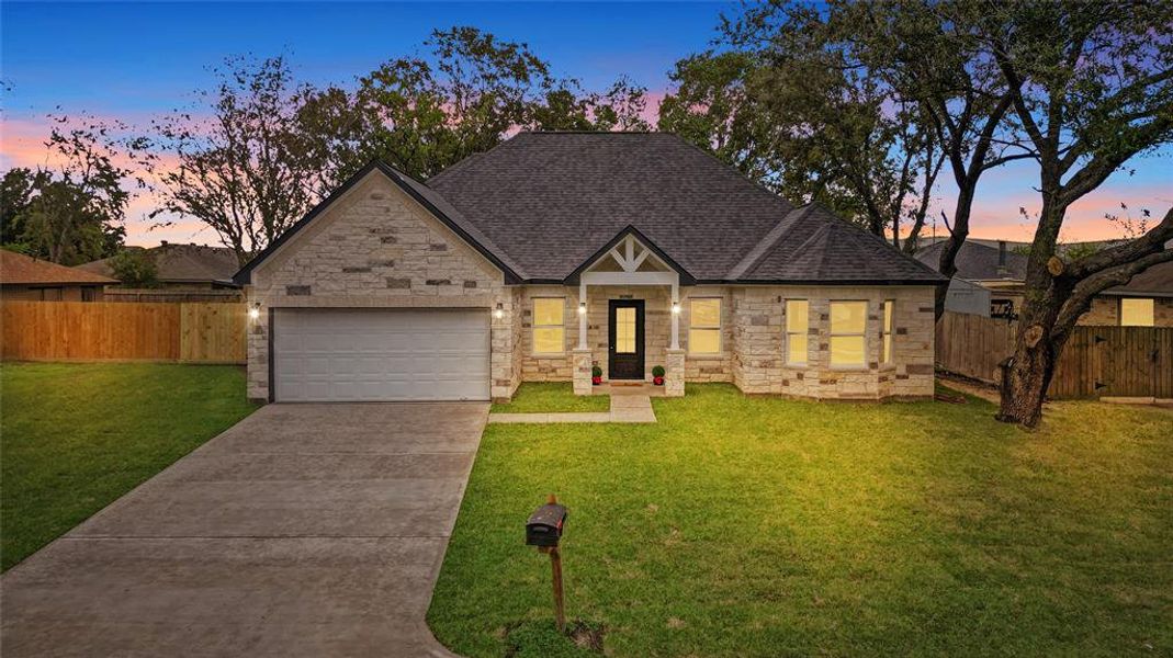 This is a single-story home featuring a stone facade, an attached two-car garage, and a well-manicured lawn. The home is captured during twilight, enhancing its curb appeal.