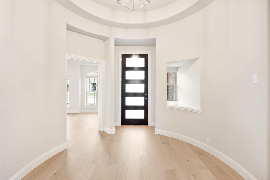 Curved foyer with round tray ceiling, dark front door with glass panels, and light hardwood floors