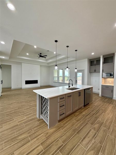 This modern open-concept living space features a spacious kitchen with a large island, pendant lighting, and ample cabinetry. The room has a stylish ceiling fan, recessed lighting, and wood-look tile flooring, creating a warm and inviting atmosphere. This modern open-concept living space features a spacious kitchen with a large island, pendant lighting, and ample cabinetry. The room has a stylish ceiling fan, recessed lighting, and wood-look tile flooring, creating a warm and inviting atmosphere.