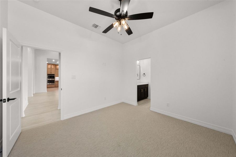 A well-lit bedroom features plush carpeting and a practical ceiling fan, with a glimpse of an adjacent bathroom. A well-lit bedroom features plush carpeting and a practical ceiling fan, with a glimpse of an adjacent bathroom.