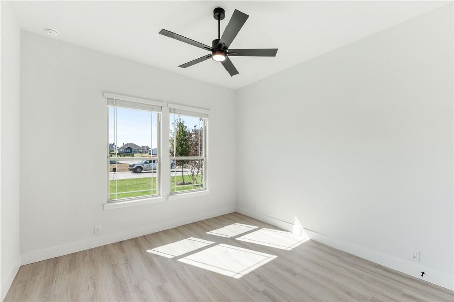 Empty room with light wood floors, white walls, black ceiling fan, and two windows with outdoor view