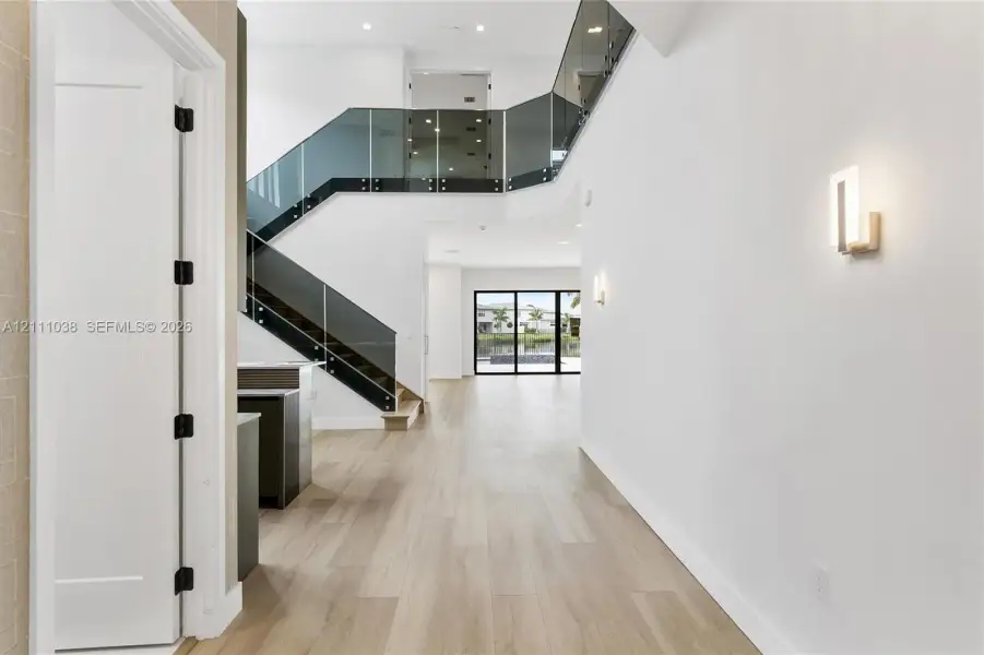 Two-story foyer featuring wood-finish flooring, a glass-paneled staircase with metal hardware, recessed lighting, and modern wall-mounted light fixtures