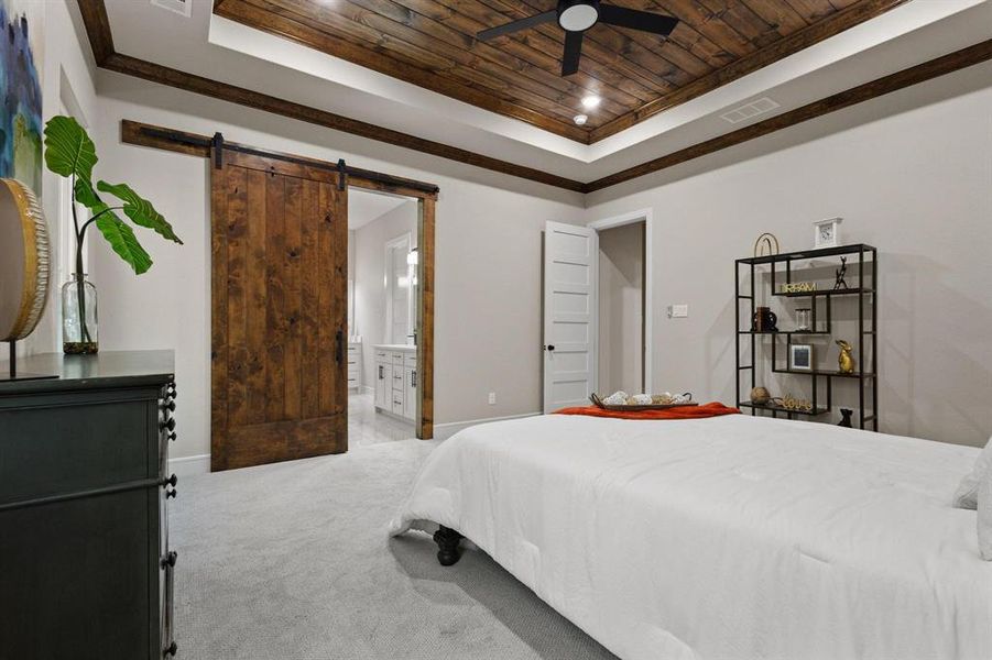 Carpeted bedroom with wooden ceiling, a tray ceiling, a ceiling fan, ensuite bathroom, and a barn door