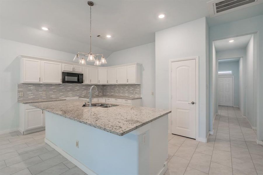 Kitchen with black microwave, backsplash, white cabinetry, light tile patterned floors, and vaulted ceiling Kitchen with black microwave, backsplash, white cabinetry, light tile patterned floors, and vaulted ceiling