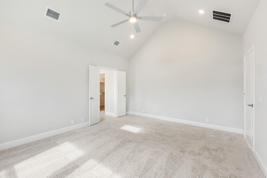 Empty bedroom with vaulted ceiling, ceiling fan, carpet flooring, and open door to ensuite bathroom