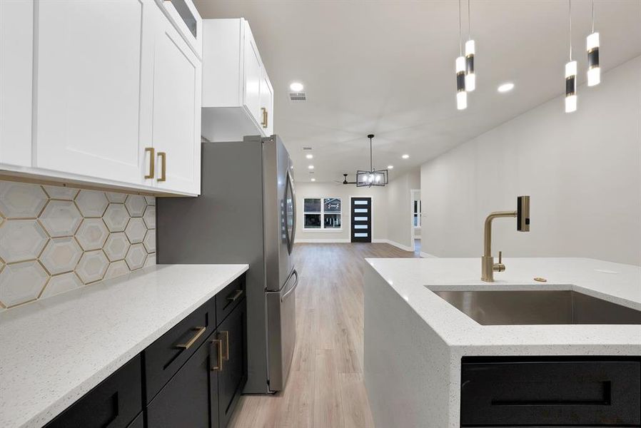Kitchen with dark cabinets, light stone countertops, light wood-type flooring, decorative light fixtures, and recessed lighting