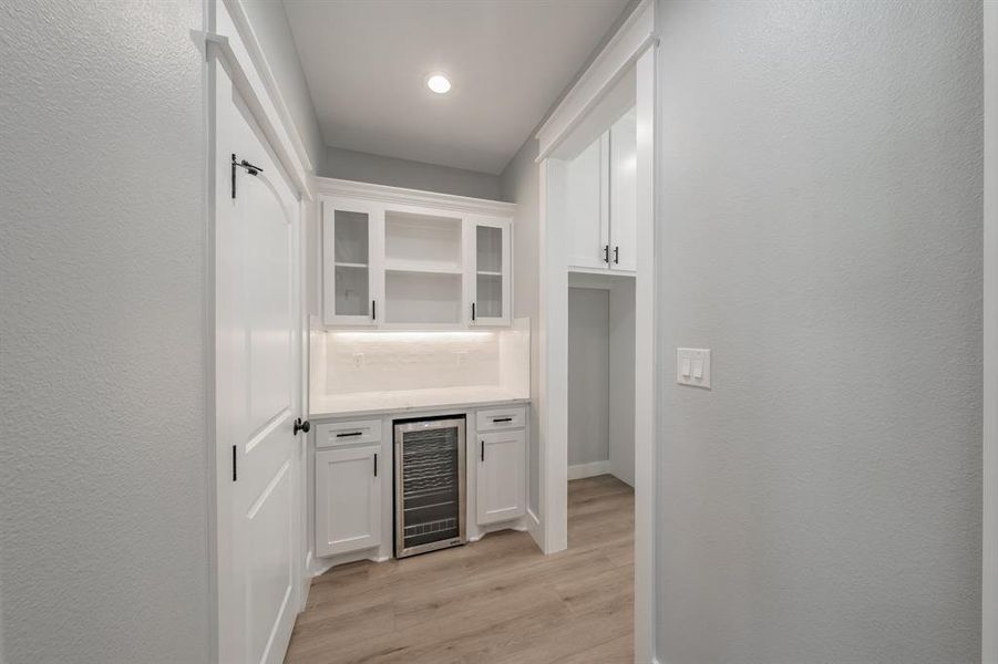 Bar with white cabinets, tasteful backsplash, beverage cooler, and light hardwood / wood-style floors