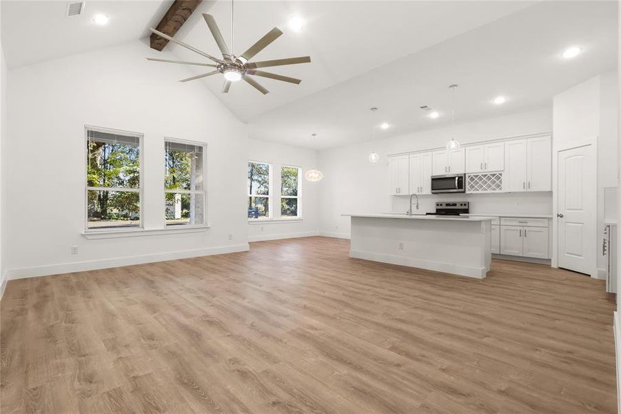 Unfurnished living room featuring high vaulted ceiling, sink, ceiling fan, beam ceiling, and light hardwood / wood-style floors