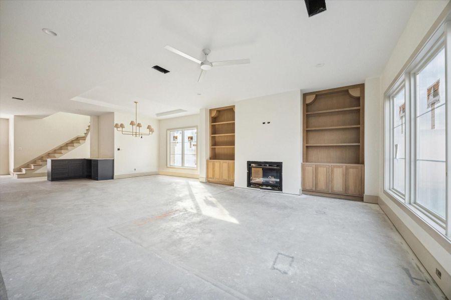 LIVING ROOM - Expansive living area features custom built in shelving, a fireplace flanked by warm wood cabinetry, and oversized windows that flood the space with natural light. Clean ceiling lines and thoughtful proportions create an open setting designed for both everyday living and effortless entertaining. -- Construction as of 1/5/26
