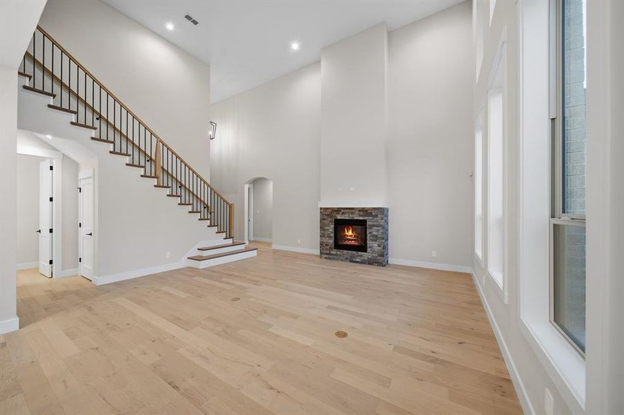 Unfurnished living room featuring a towering ceiling, light wood-type flooring, a fireplace, recessed lighting, and arched walkways