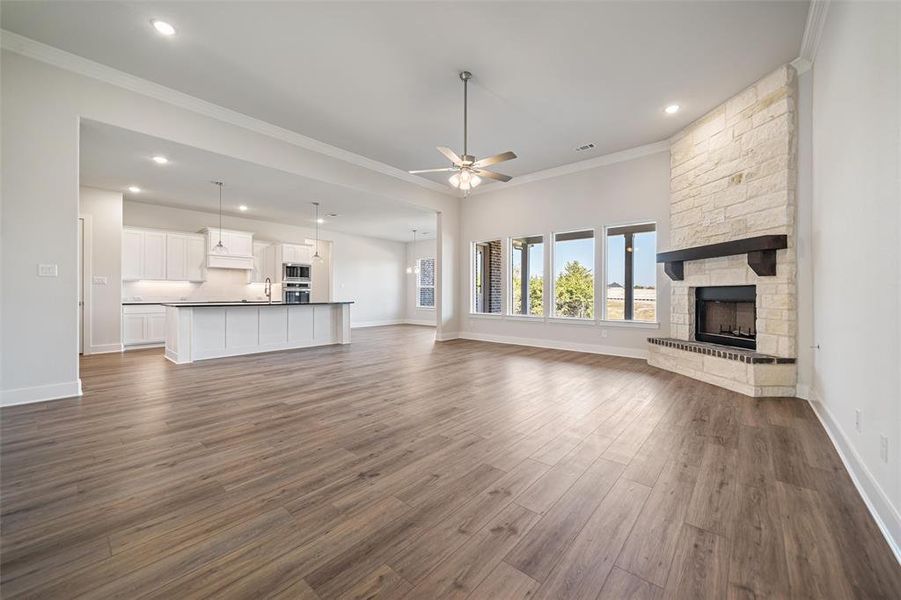 Unfurnished living room featuring ornamental molding, a stone fireplace, a ceiling fan, dark wood-type flooring, and recessed lighting Unfurnished living room featuring ornamental molding, a stone fireplace, a ceiling fan, dark wood-type flooring, and recessed lighting